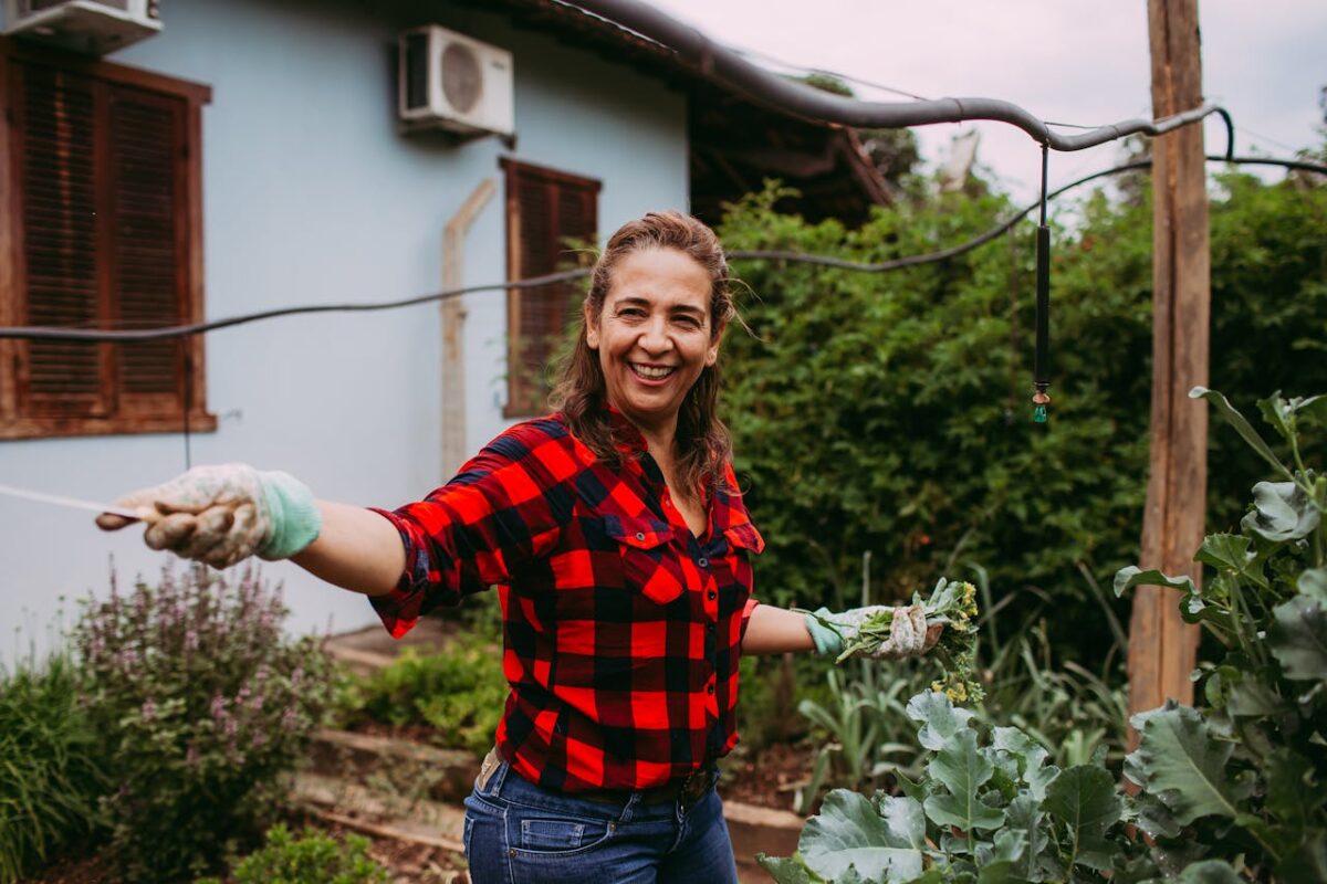 A happy woman in plaid shirt tends her garden, showcasing a vibrant, serene outdoor lifestyle.